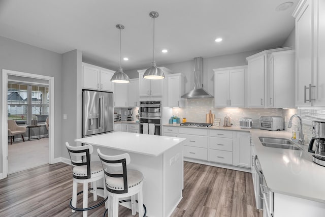 kitchen with wall chimney exhaust hood, a kitchen island, appliances with stainless steel finishes, a kitchen breakfast bar, and a sink