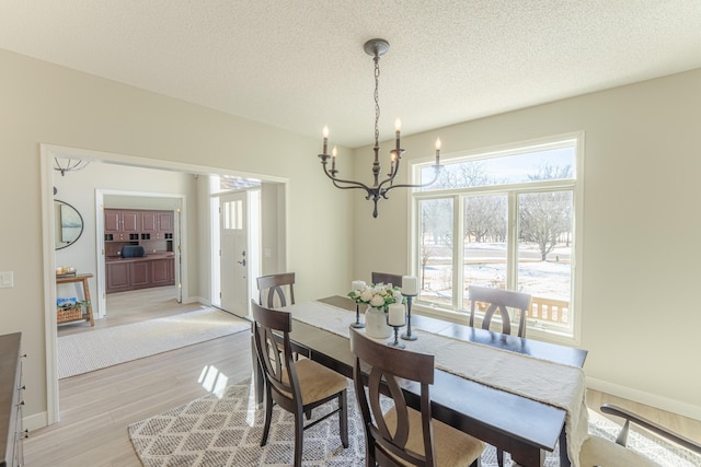 dining room with light wood-style flooring, a notable chandelier, baseboards, and a textured ceiling