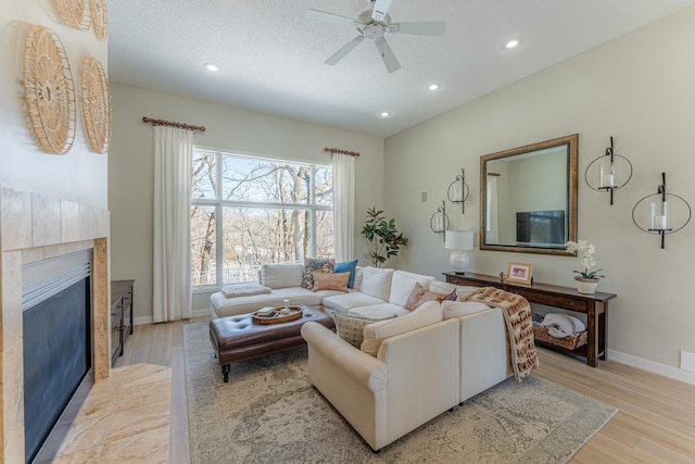 living area featuring light wood-type flooring, a textured ceiling, recessed lighting, baseboards, and a tile fireplace