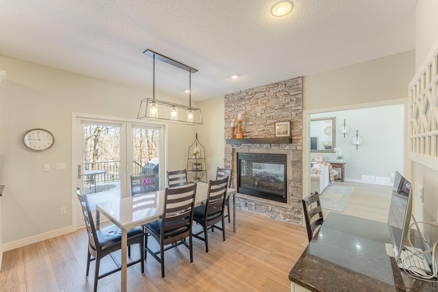 dining area with baseboards, a textured ceiling, a fireplace, and light wood finished floors