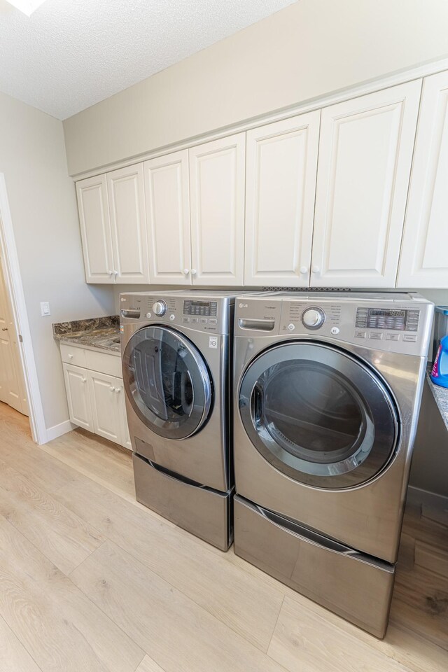 clothes washing area with washer and clothes dryer, a textured ceiling, cabinet space, light wood finished floors, and baseboards