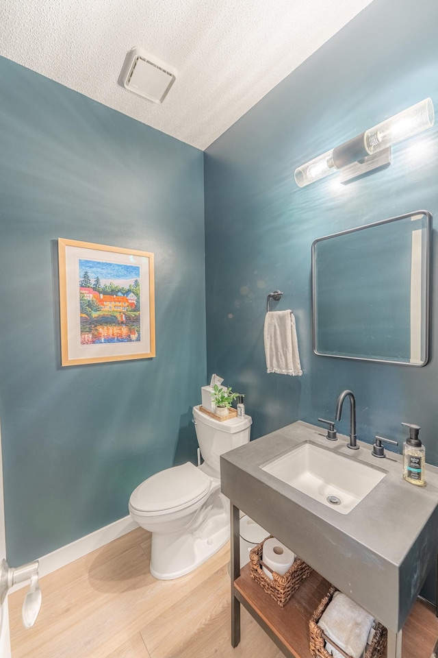 bathroom featuring visible vents, baseboards, toilet, wood finished floors, and a sink