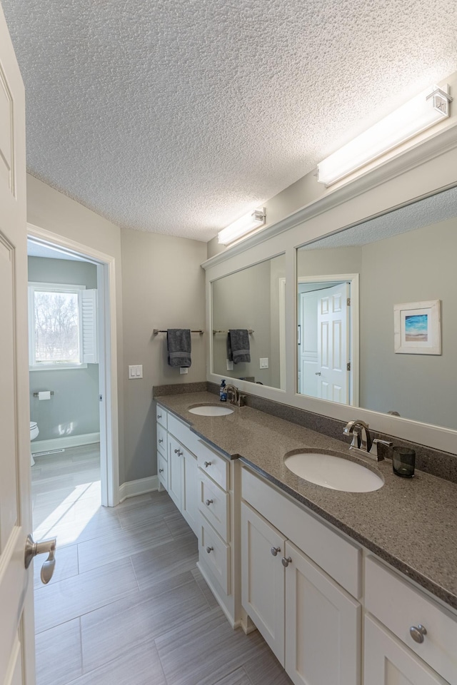 full bathroom with a sink, toilet, double vanity, and a textured ceiling