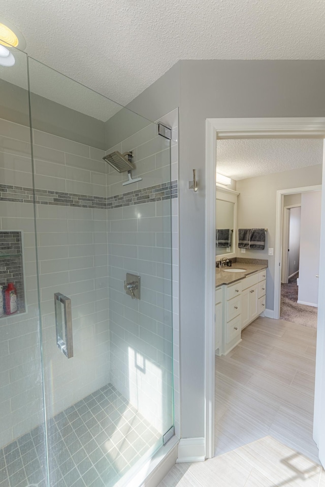 full bathroom featuring baseboards, a stall shower, vanity, and a textured ceiling