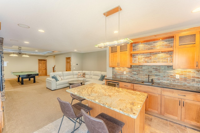 kitchen featuring a sink, a kitchen breakfast bar, tasteful backsplash, a center island, and light stone countertops