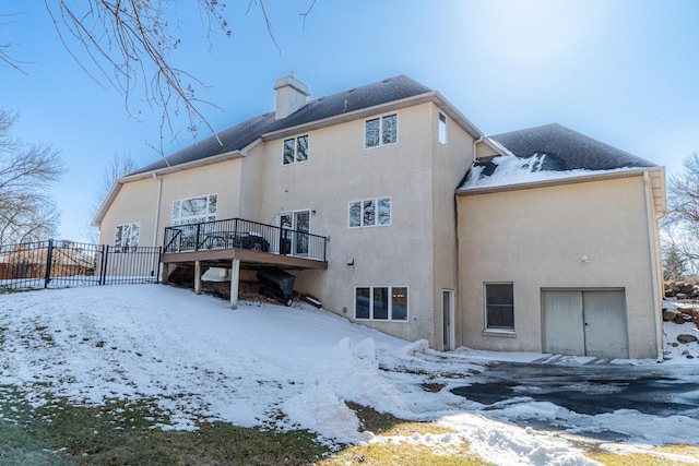 snow covered back of property with stucco siding, fence, and a chimney