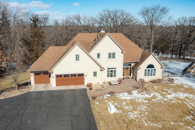 view of front of property featuring roof with shingles, driveway, stucco siding, a chimney, and a garage