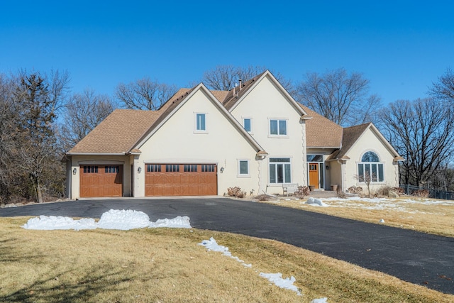 view of front facade with roof with shingles, stucco siding, a front lawn, a garage, and aphalt driveway