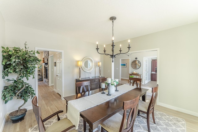 dining space with a chandelier, baseboards, a textured ceiling, and light wood-style flooring