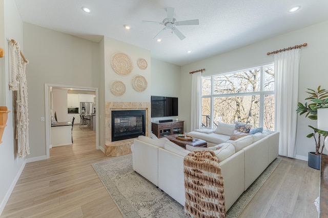 living room with a tiled fireplace, recessed lighting, light wood-style flooring, and baseboards