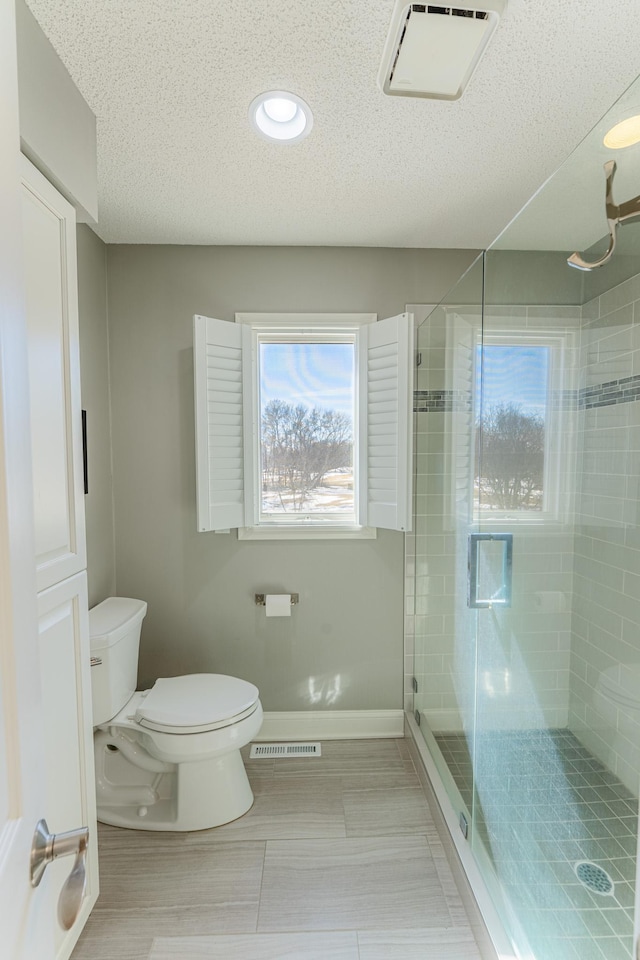 bathroom featuring visible vents, toilet, a textured ceiling, a shower stall, and baseboards