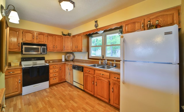 kitchen with a sink, white appliances, light wood-style floors, and brown cabinets