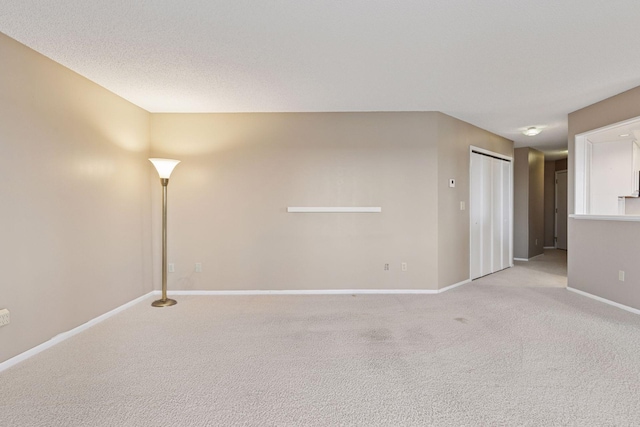 empty room with a textured ceiling, baseboards, and light carpet