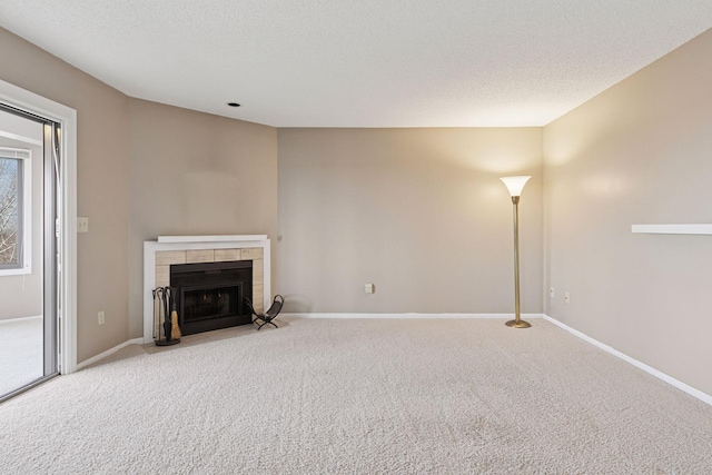 unfurnished living room featuring baseboards, a textured ceiling, carpet flooring, and a tile fireplace