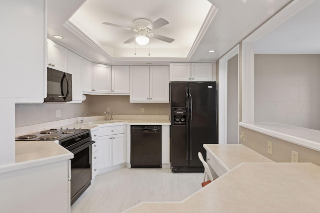 kitchen with a tray ceiling, a sink, black appliances, white cabinets, and light countertops