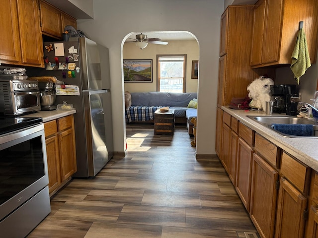 kitchen featuring arched walkways, brown cabinetry, appliances with stainless steel finishes, light countertops, and a sink