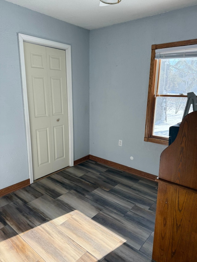 unfurnished bedroom with dark wood-style flooring, a closet, and baseboards