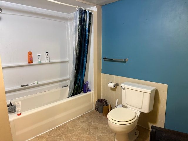 bathroom with toilet, a wainscoted wall, shower / bath combo, and tile walls