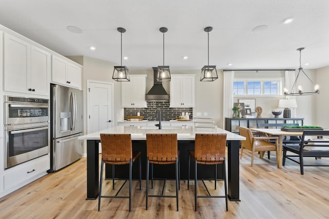 kitchen featuring light countertops, custom range hood, decorative backsplash, appliances with stainless steel finishes, and light wood-style floors