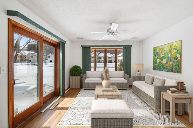 living room featuring a textured ceiling, light wood finished floors, visible vents, and a ceiling fan