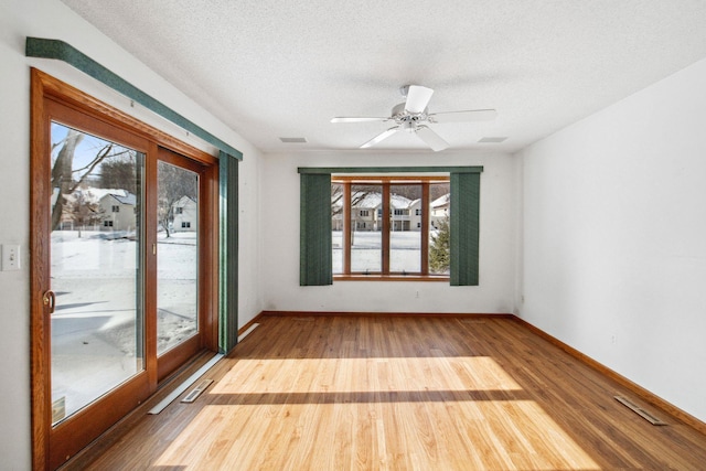 empty room featuring visible vents, a textured ceiling, baseboards, and wood finished floors