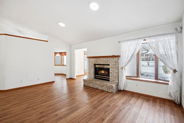 unfurnished living room with vaulted ceiling, a brick fireplace, wood finished floors, and baseboards