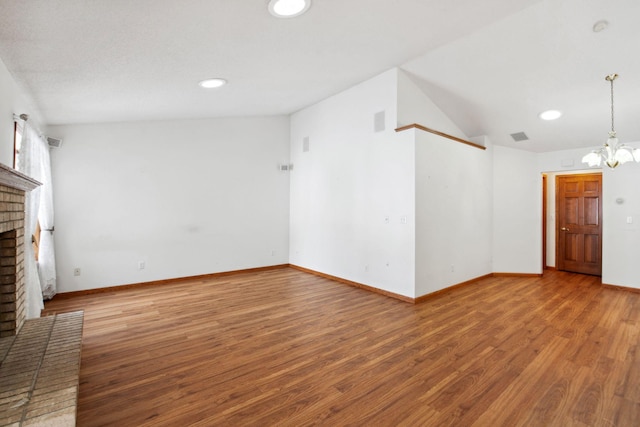 unfurnished living room featuring lofted ceiling, a brick fireplace, a notable chandelier, and wood finished floors