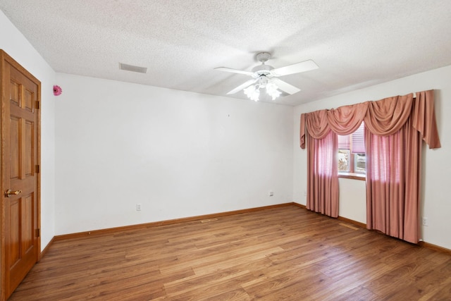 empty room with visible vents, light wood finished floors, a textured ceiling, and a ceiling fan