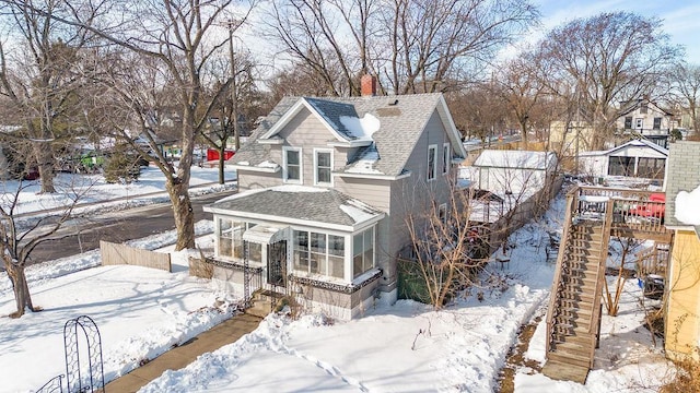 view of snowy exterior featuring a chimney, a shingled roof, stairway, a sunroom, and fence