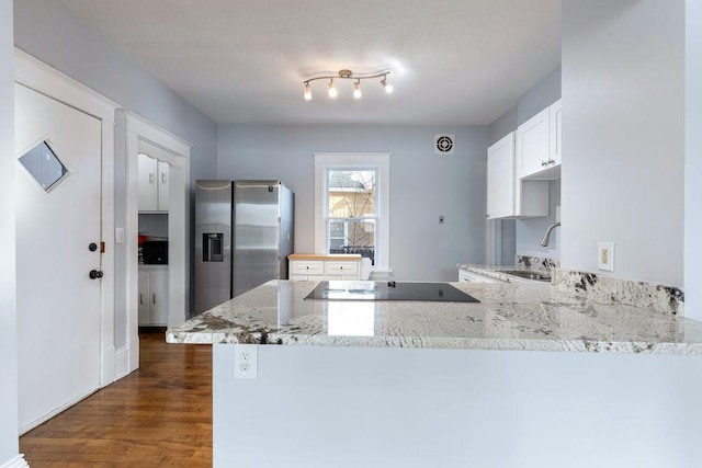 kitchen featuring black electric stovetop, light stone counters, a peninsula, a sink, and stainless steel fridge