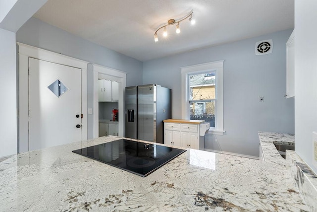 kitchen featuring visible vents, light stone countertops, black electric cooktop, and stainless steel fridge with ice dispenser