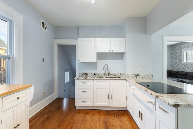 kitchen featuring black electric stovetop, wood finished floors, white cabinetry, a sink, and light stone countertops