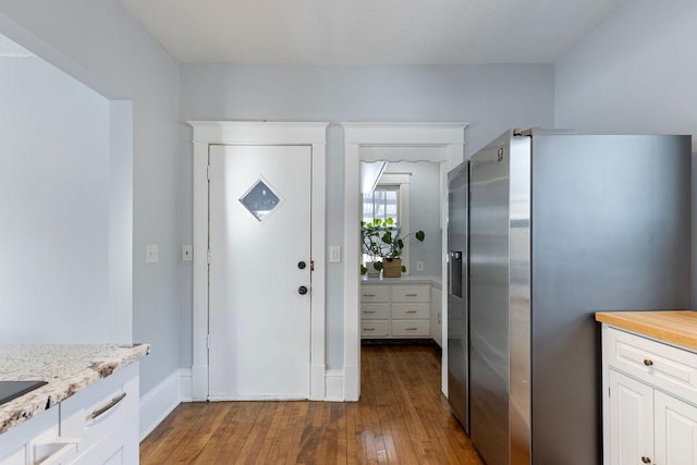 kitchen featuring light stone countertops, white cabinetry, stainless steel refrigerator with ice dispenser, and dark wood-type flooring