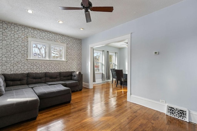 living room with visible vents, an accent wall, a textured ceiling, baseboards, and hardwood / wood-style flooring