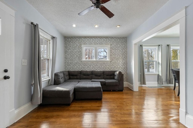 living area with an accent wall, wood finished floors, a wealth of natural light, and wallpapered walls