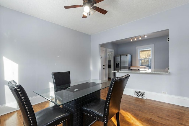 dining space featuring ceiling fan, a textured ceiling, wood finished floors, visible vents, and baseboards