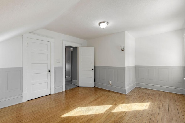 bonus room featuring light wood-type flooring, a wainscoted wall, a textured ceiling, and lofted ceiling