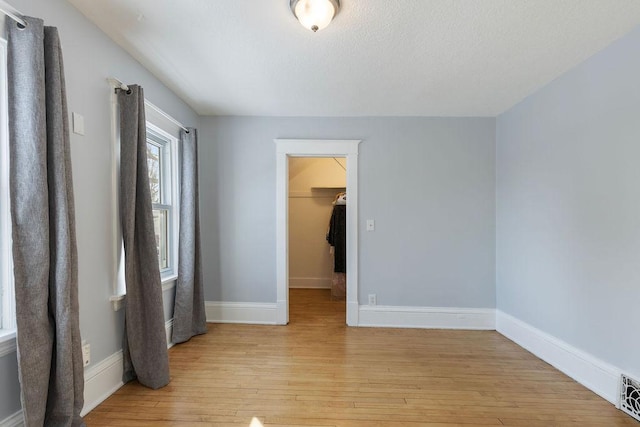 interior space featuring light wood-type flooring, a walk in closet, visible vents, and baseboards