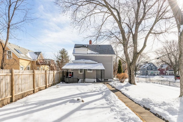 snow covered rear of property with fence and a chimney