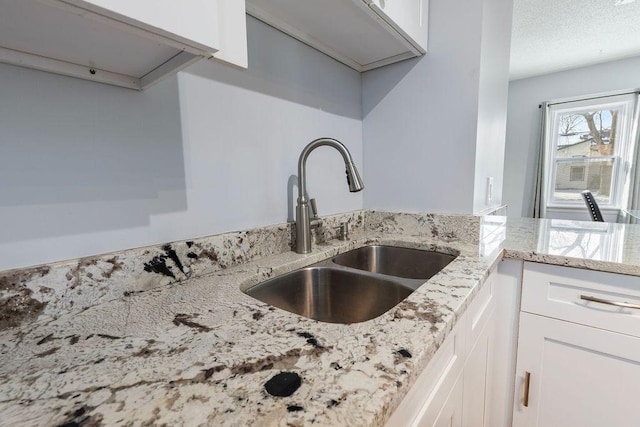 kitchen with light stone counters, white cabinets, and a sink