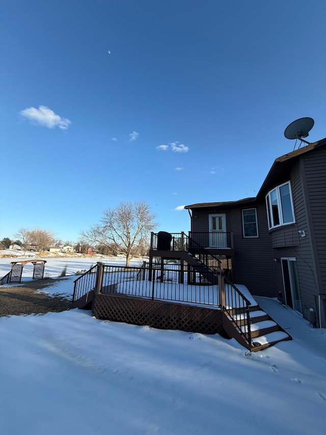 snow covered back of property featuring stairway and a wooden deck