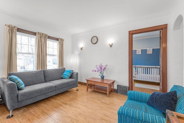 living area featuring baseboards, crown molding, light wood-style floors, and a textured wall