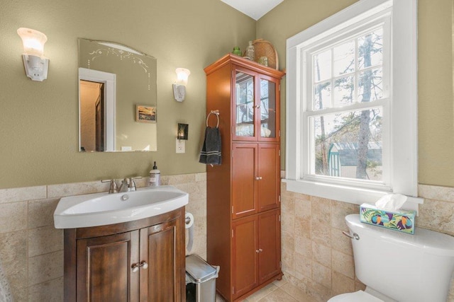 bathroom with a wainscoted wall, toilet, tile walls, tile patterned flooring, and vanity