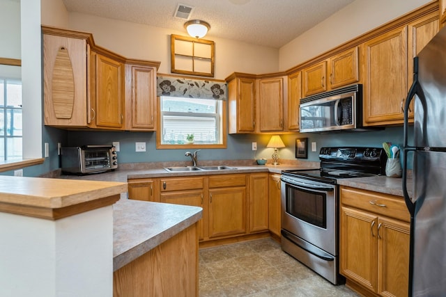 kitchen with visible vents, a sink, a textured ceiling, stainless steel appliances, and a toaster