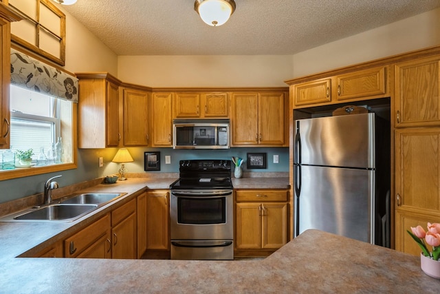 kitchen with a sink, stainless steel appliances, a textured ceiling, and brown cabinetry