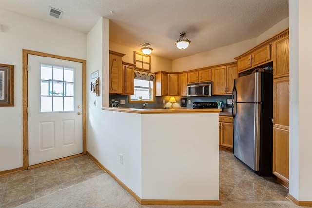 kitchen featuring brown cabinetry, visible vents, a peninsula, stainless steel appliances, and a textured ceiling