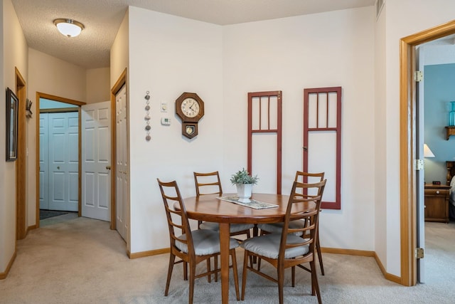 dining space featuring light colored carpet, a textured ceiling, and baseboards