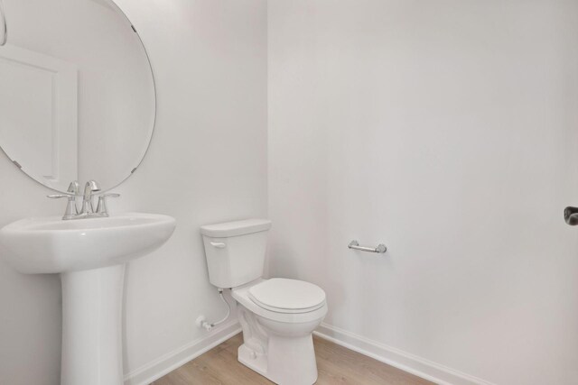 half bath featuring baseboards, a sink, toilet, and wood finished floors