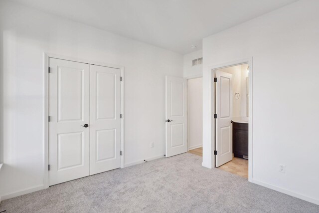 unfurnished bedroom featuring connected bathroom, light colored carpet, visible vents, baseboards, and a closet