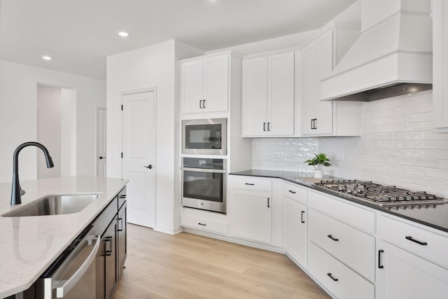 kitchen featuring light wood-style flooring, appliances with stainless steel finishes, a sink, light stone countertops, and premium range hood